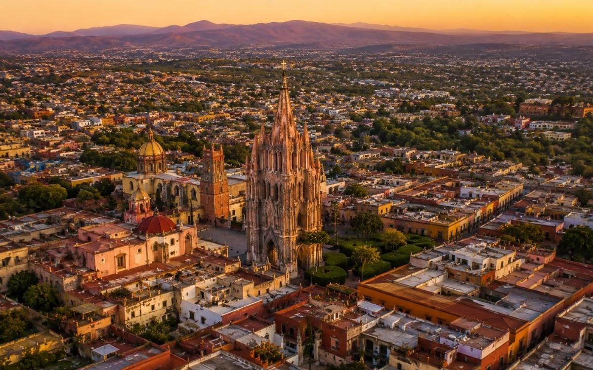 Aerial view of San Miguel de Allende colonial rooftops at golden hour with the pink Parroquia cathedral rising from the center