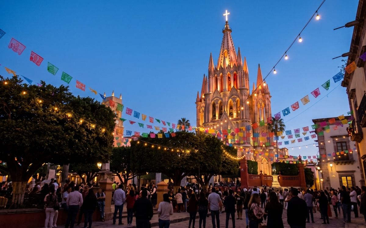 San Miguel de Allende's Jardín Principal at twilight during a festival with warm lights, papel picado, and the illuminated Parroquia